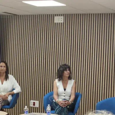 Dos mujeres sentadas en un panel frente a pantallas rojas.