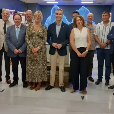 Grupo de personas de distintasedades y géneros, de pie en fila, en interior con fondo azul y luces.