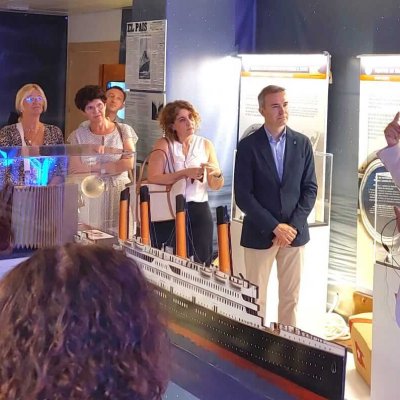 Un guía con bata blanca explica una maqueta a visitantes en un museo.