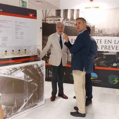 Dos hombres en un stand expositivo; uno entrevista al otro con micrófono.