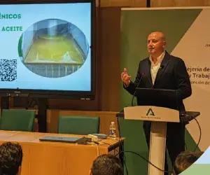 Fotografía de un conferenciante en escenario con pantalla y gráfico de ponente en podio.