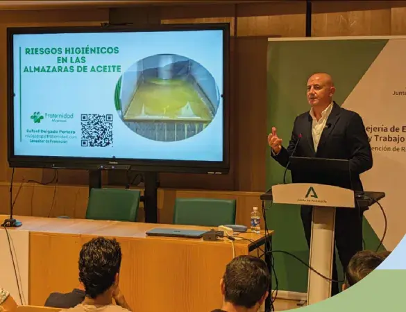 Fotografía de un conferenciante en escenario con pantalla y gráfico de ponente en podio.