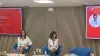 Dos mujeres sentadas en un panel frente a pantallas rojas.