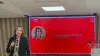 Mujer con micrófono frente a pantalla roja con foto y texto