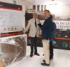 Dos hombres en un stand expositivo; uno entrevista al otro con micrófono.