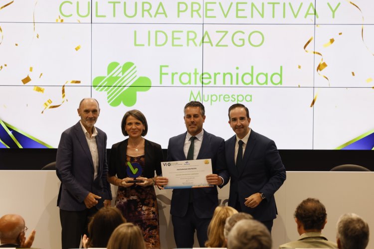 Cuatro personas en un escenario, dos hombres sostienen un certificado, fondo con texto y logo.